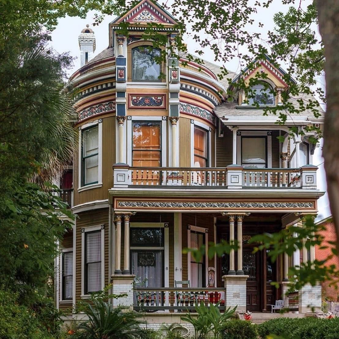 Multi-story Victorian house with ornate trim, bay windows, and porch surrounded by green trees