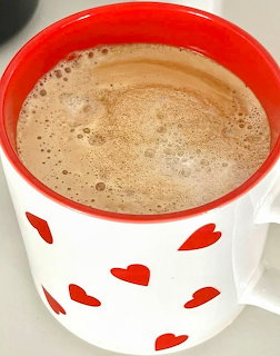 Frothy coffee in a white mug with red heart patterns