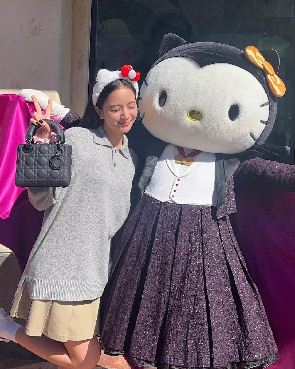 Young woman smiling next to a life-sized Hello Kity mascot in a glittery purple skirt outdoors
