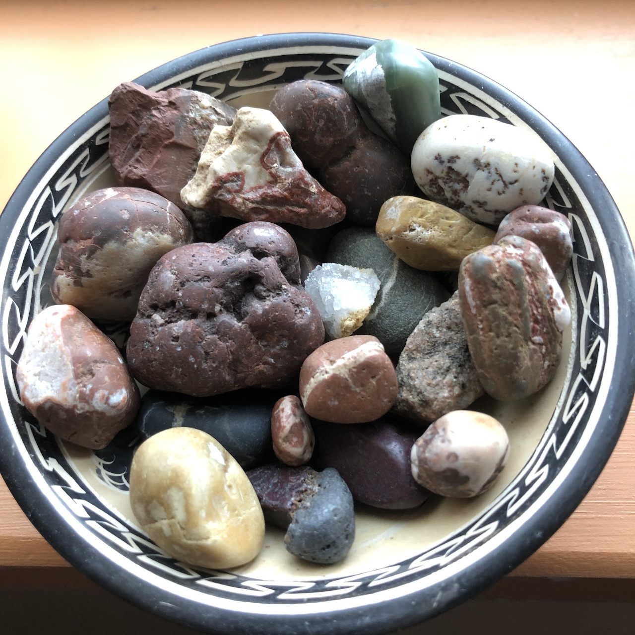 Patterned bowl filled with assorted smooth stones and pebbles in earthy colors