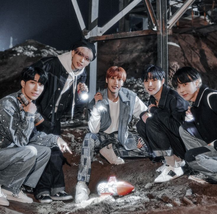 Five young men posing together in a rocky industrial setting with reflective outfits