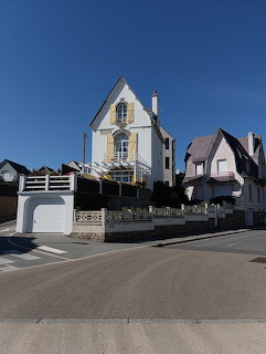 Tall yellow and white house beside a quiet street under a clear blue sky