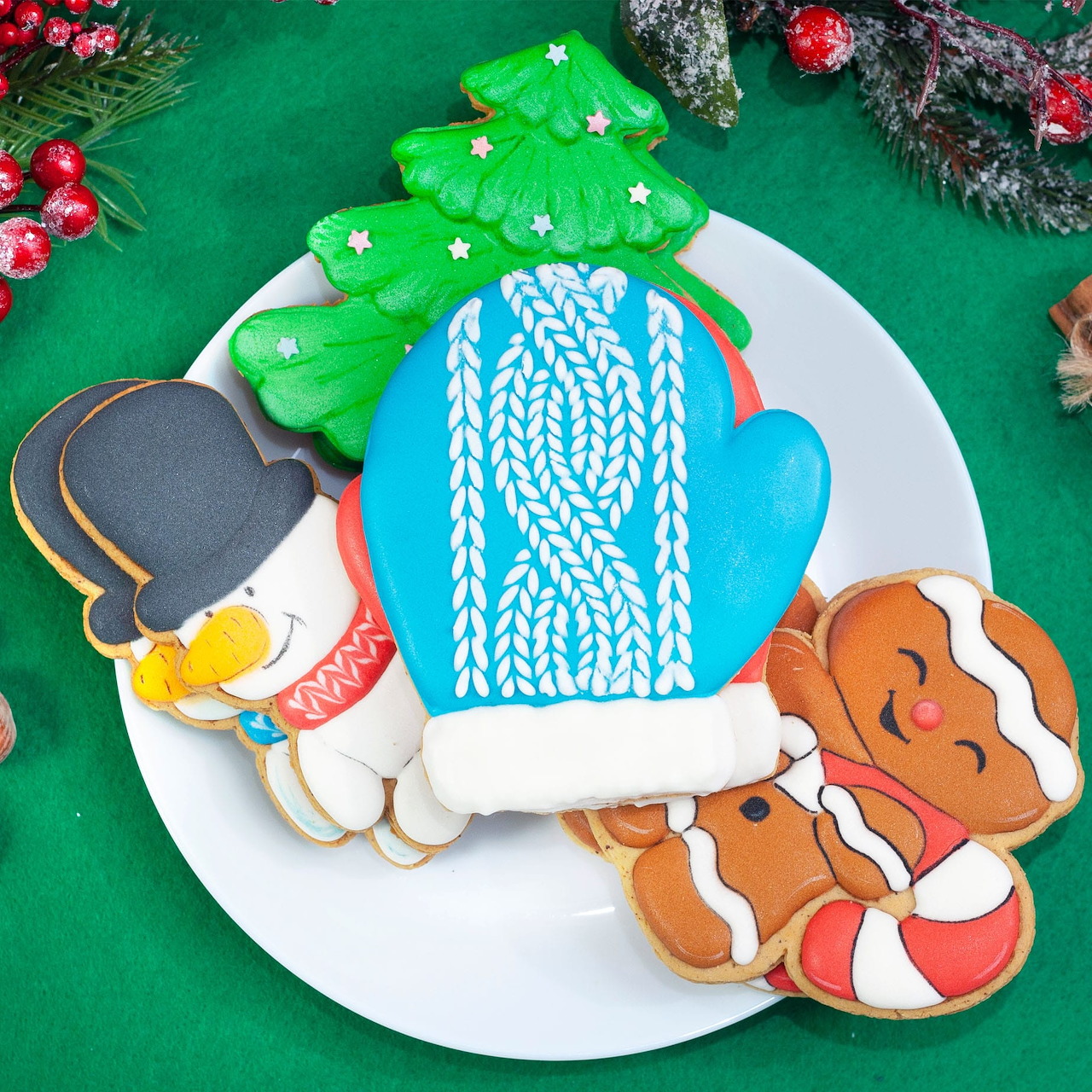 Christmas cookies on a white plate, including a blue mitten, tree, snowman, gingerbread cookie, and candy cane