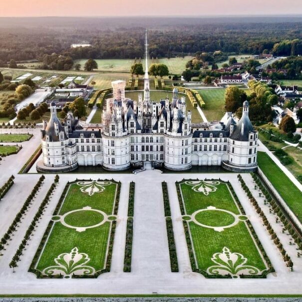 Aerial view of a large French castle with symmetrical formal gardens and surrounding countryside