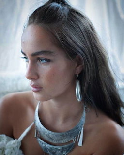 Close-up portrait of a young woman with brown hair, blue eyes, silver choker necklace and drop earrings