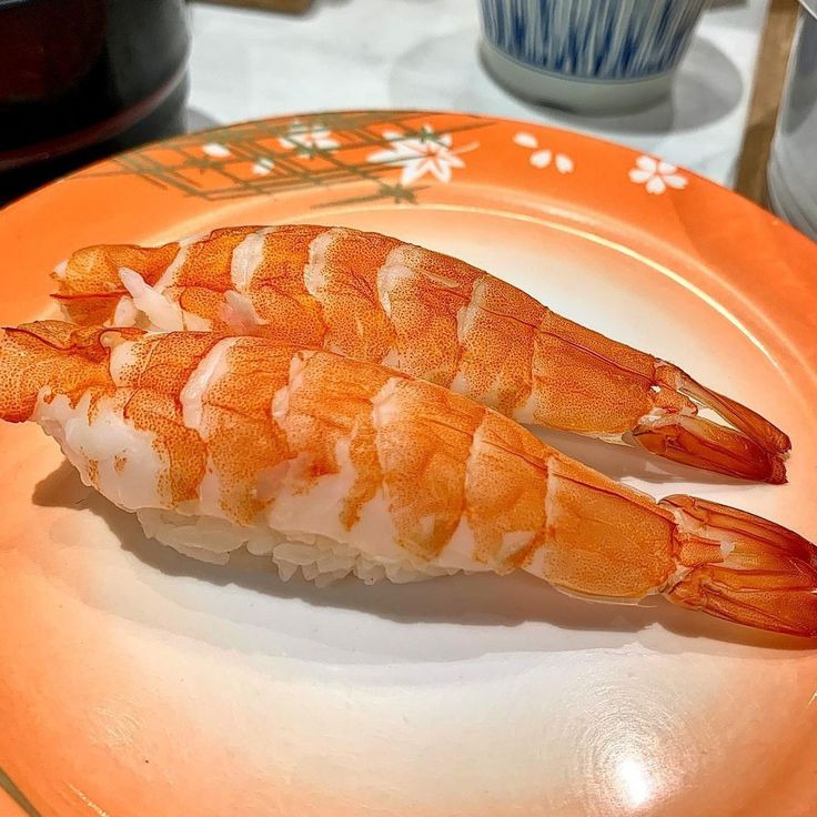 Shrimp nigiri sushi on orange floral plate with striped teacup in background