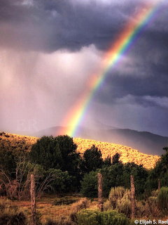Rainbow over desert landscape with stormy clouds and golden sunlit hills in New Mexico
