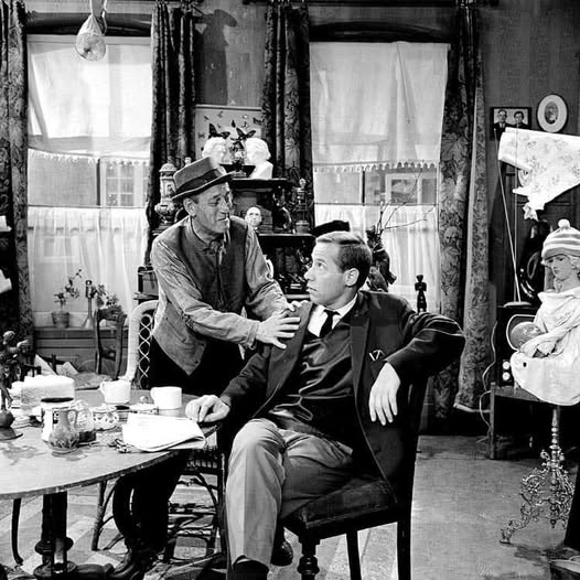 Black and white photo of three people in a 1950s Dutch living room with vintage furniture and curtained windows