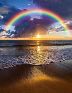 Double rainbow over ocean beach at sunset with breaking waves and golden sand