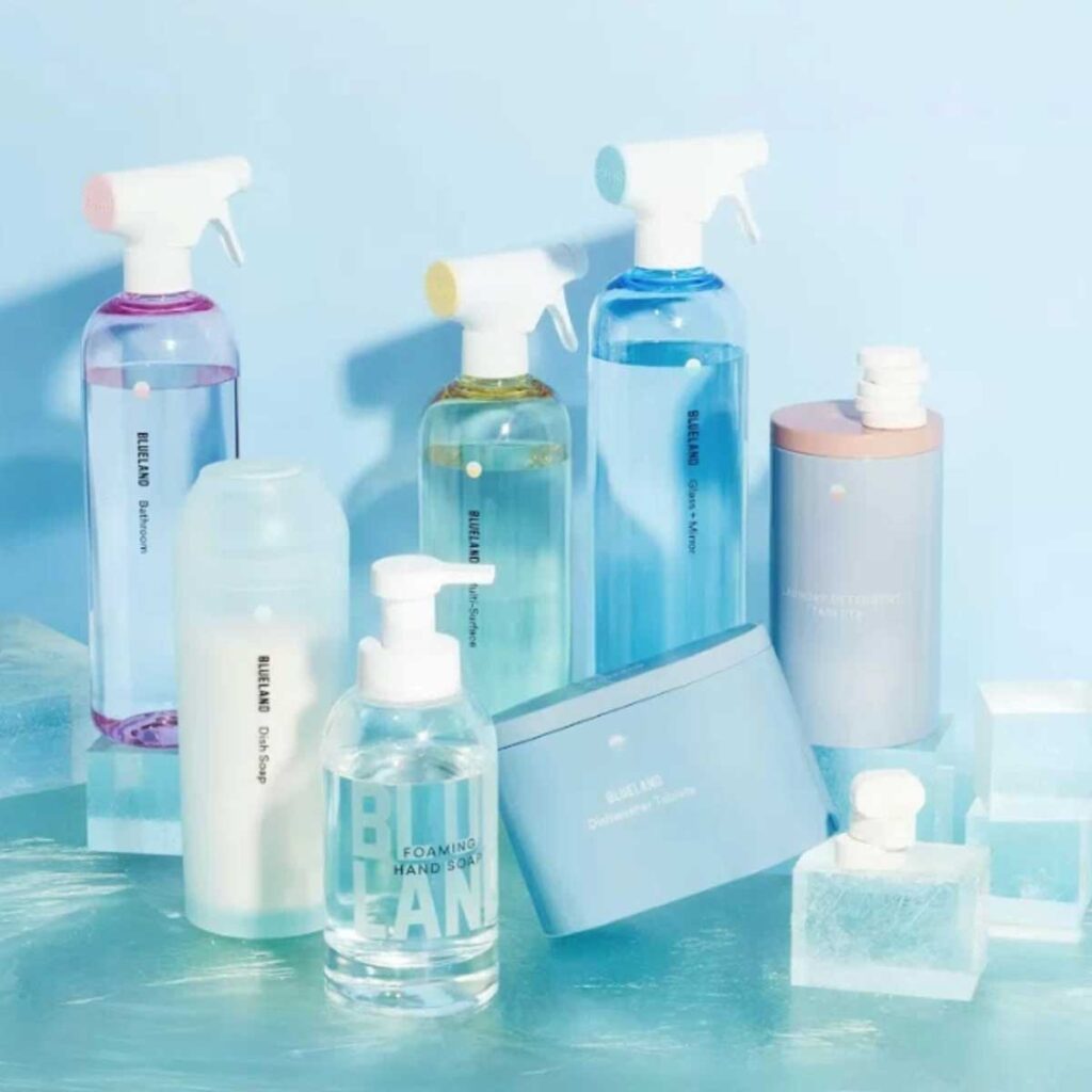 Assorted pastel cleaning bottles and containers arranged aesthetically on blue surface
