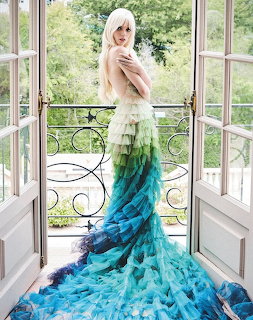 Woman in dramatic turquoise ombre feather gown on balcony overlooking garden