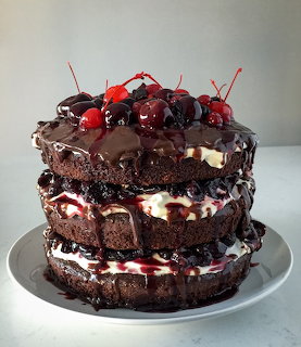 Three-layer chocolate cake topped with fresh cherries and chocolate drizzle on grey plate