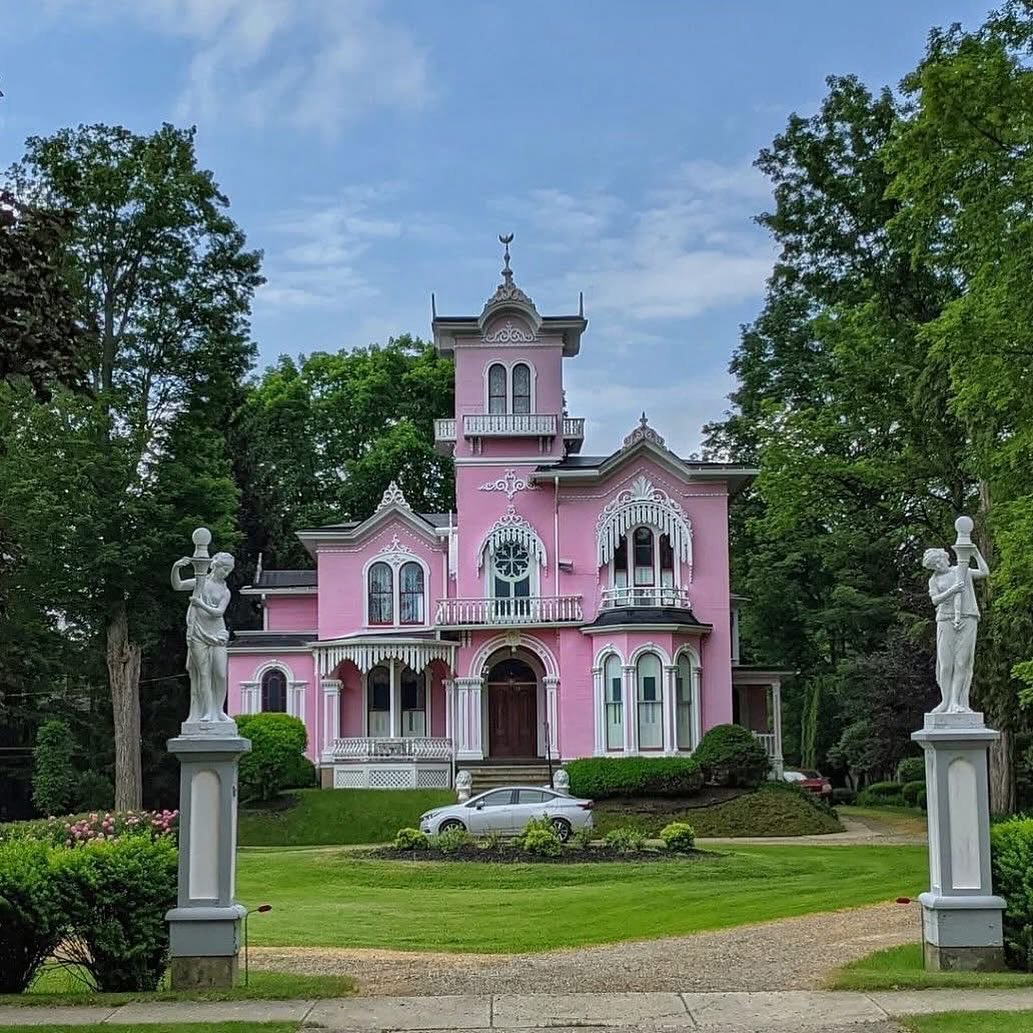 Pink Victorian mansion with tower and white statues on green lawn