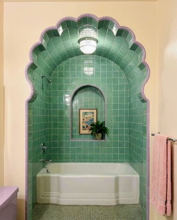 Vintage art deco bathroom with green tiled arch over white bathtub, scalloped trim, and pink towel