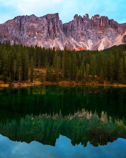 Jagged Dolomite mountain peaks perfectly reflected in calm green alpine lake with pine forest shore