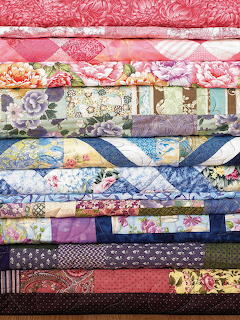 Horizontal stack of colorful quilted fabric layers with diverse floral and geometric patterns