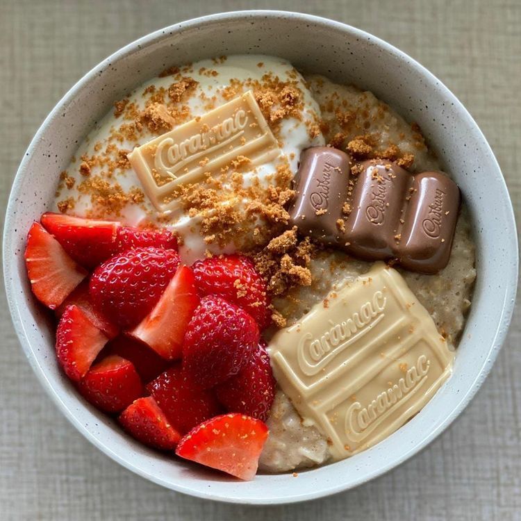 Bowl of creamy oats topped with strawberries, chocolate pieces, and crumbs