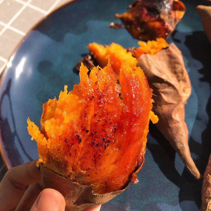Hand holding a baked sweet potato split open showing bright orange caramelized flesh