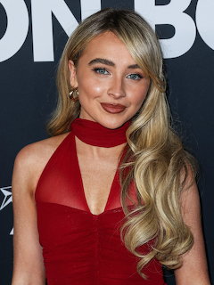 Sabrina Carpenter posing in a red dress with long blonde hair at an event backdrop