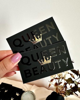 Hand holding two black cards reading Queen Beauty with small gold crown decorations