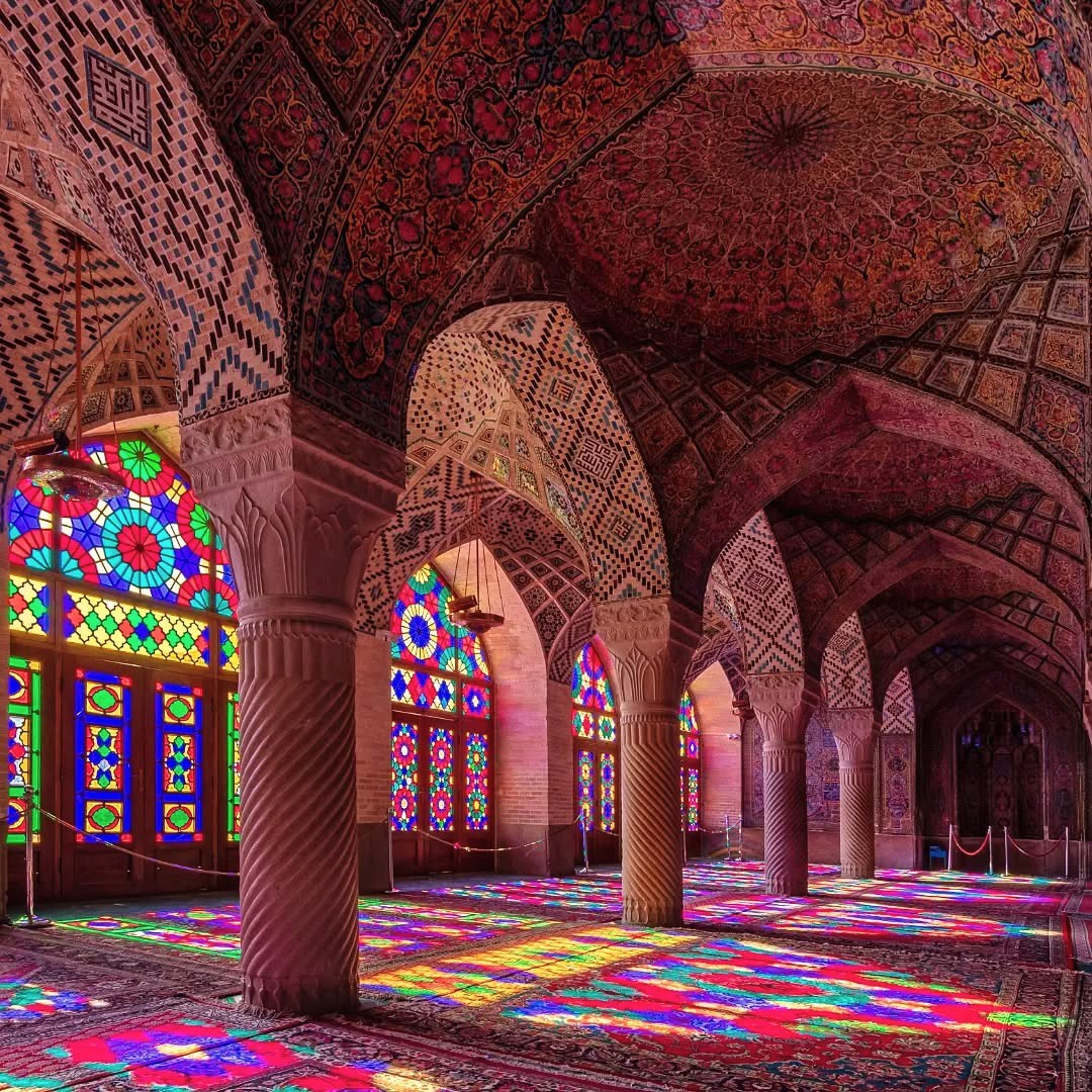 Ornate mosque interior with colorful stained glass windows and patterned vaulted ceilings casting vibrant reflections
