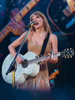 Blonde singer in gold sequined dress playing sparkling guitar and singing into a microphone on stage