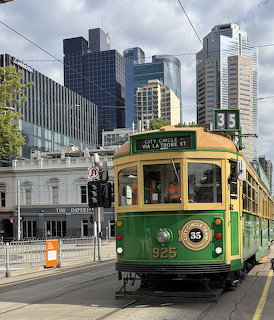 Green and yellow vintage Melbourne tram 925 on city street with skyscrapers behind