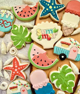 Assortment of decorated sugar cookies with summer themes like watermelon, starfish, tropical leaves, and beach camper