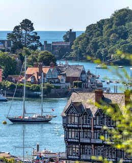 Dartmouth harbour with sailboat, historic buildings, green hills, and boats on the River Dart