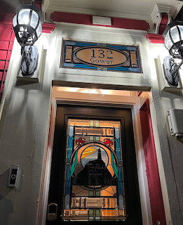 Decorative front door with stained glass panel and transom window reading 132 Gower, flanked by two wall lanterns