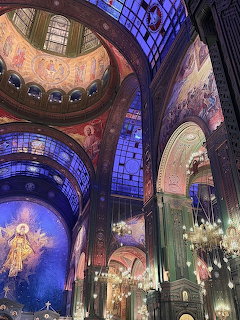 Ornate interior of a Russian Orthodox cathedral with painted domes, frescoes, stained glass, and chandeliers