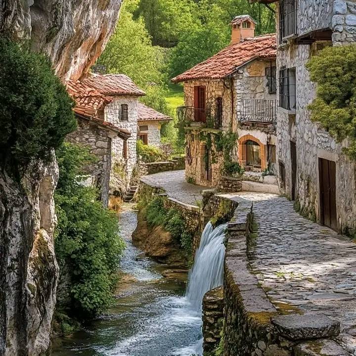 Historic Spanish village with stone buildings and stream flowing through cobblestone path