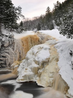 Snowy Rainbow Falls waterfall with ice-covered rocks and trees in winter