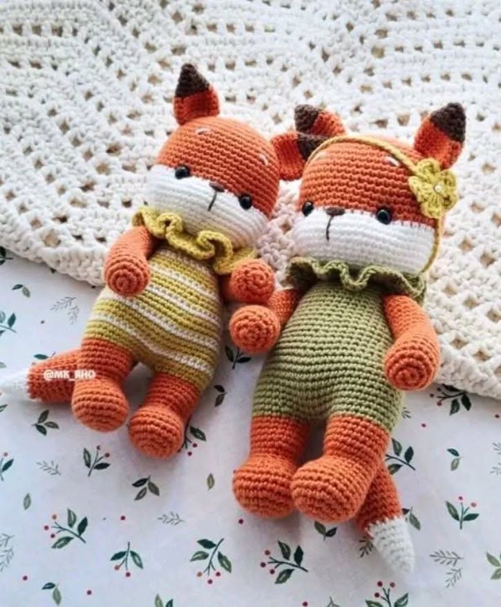 Two crocheted amigurumi fox dolls on floral fabric next to a white knitted blanket