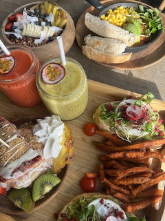 Overhead view of a brunch table with colorful smoothies, acai bowl, sandwiches, and sweet potato fries on wooden boards