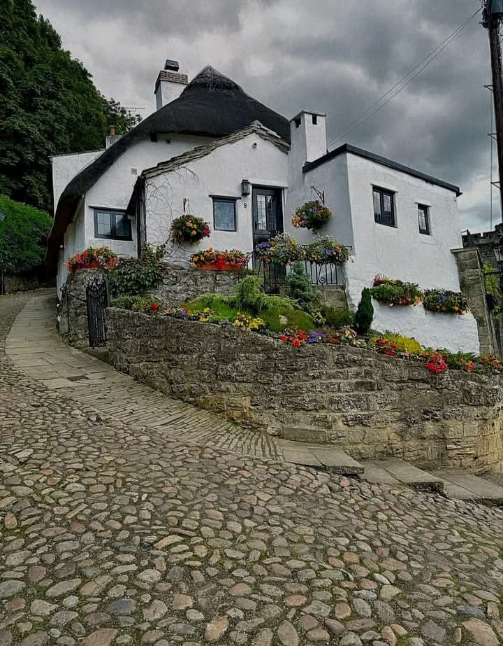 White thatched cottage with flower boxes along a cobblestone street and stone wall