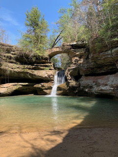 Natural stone arch bridge over a waterfall flowing into a turquoise pool surrounded by sandstone cliffs