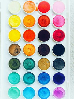 Organized grid of colorful paint pigments in white circular containers on light surface