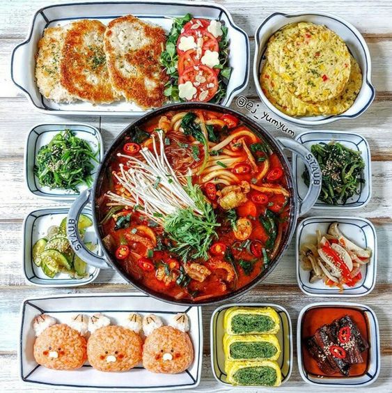 Overhead photo of Korean meal with stew, pancakes, and various side dishes in bowls and plates on wooden table