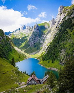 Alpine lake nestled between dramatic mountain cliffs with a chalet on green slopes under blue sky