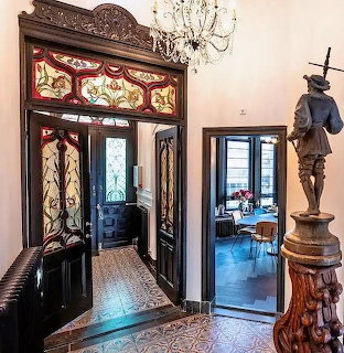 Ornate Art Nouveau hallway with stained glass, carved wood doorway, mosaic floor, bronze statue and chandelier
