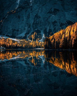 Alpine lake mirroring golden autumn forest and dramatic mountain peaks in dark blue water