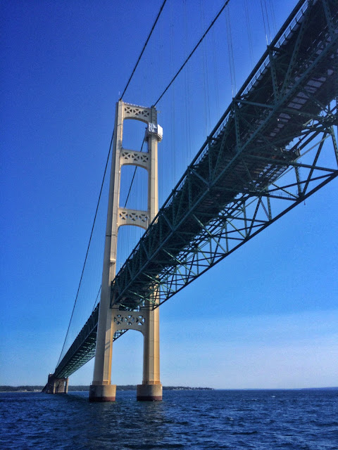 Low-angle view of a Mackinac Bridge suspension tower against a clear blue sky over open water