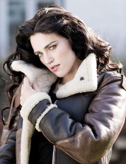 Woman with dark wavy hair in brown shearling jacket looking at camera