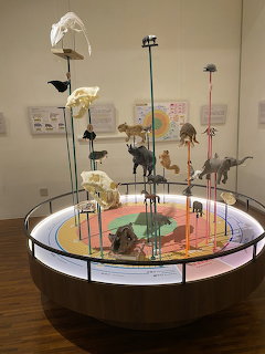 Circular museum display table with animal figurines and bone models on stands in a gallery
