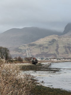 Shipwreck on rocky shoreline with misty Scottish highlands and mountains in the background