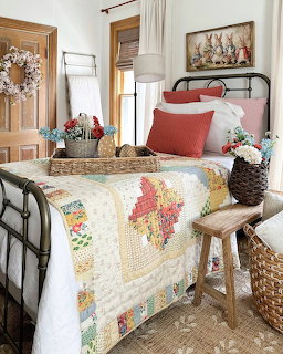 Cottage bedroom with iron bed, patchwork quilt, coral pillows, wicker baskets, and spring buny artwork