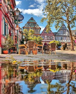 Half-timbered buildings and café seating in Idstein, Germany, reflected in a puddle