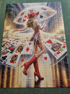 Woman in red boots and hat holding a clear umbrella with playing cards scattered around her in the rain