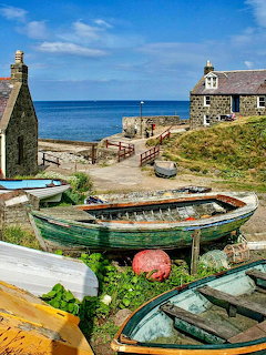 Old fishing boats on beach with stone cottages and ocean view under blue sky